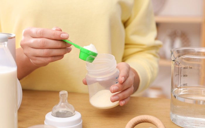 A close-up of a woman's hands preparing a bottle of infant formula milk