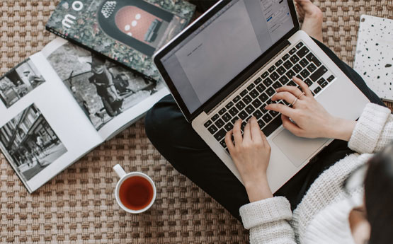 A person using a laptop surrounded by books 