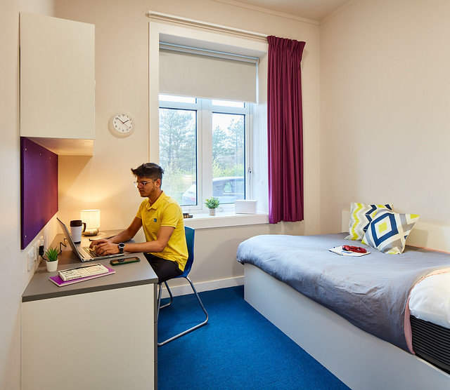 Male student sitting at desk in bedroom.