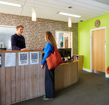 An image of a student talking to a member of staff at an Estates reception desk on campus.