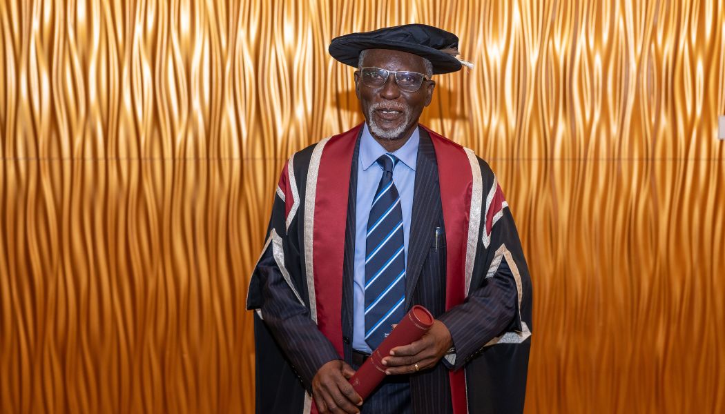 Man wearing cap & gown and holding a scroll