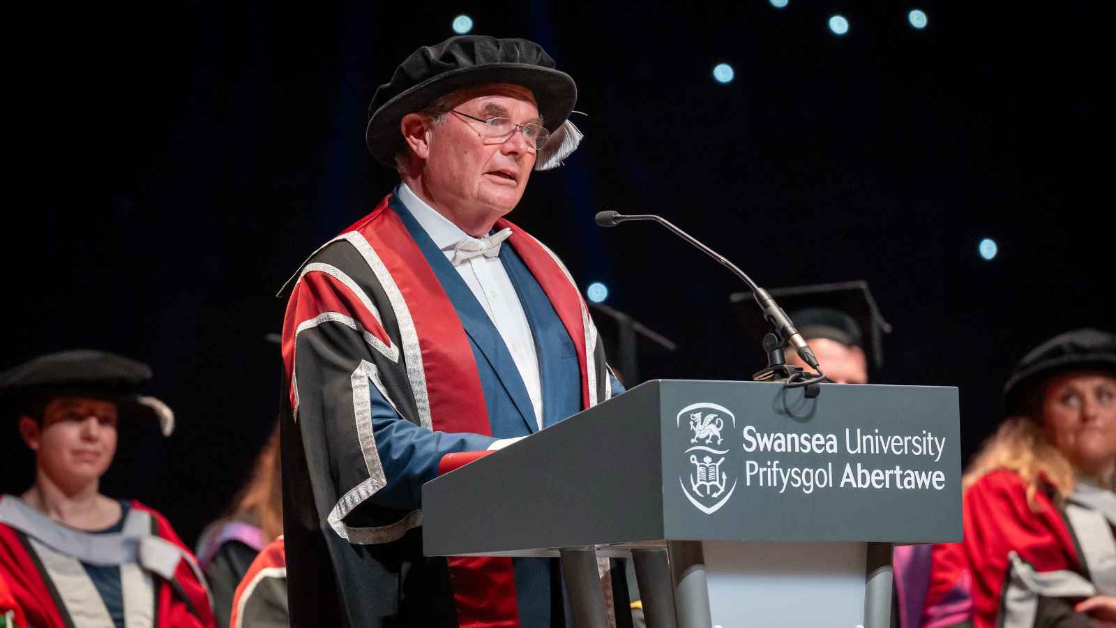 Man standing behind a lectern making a speech dressed in cap and gown