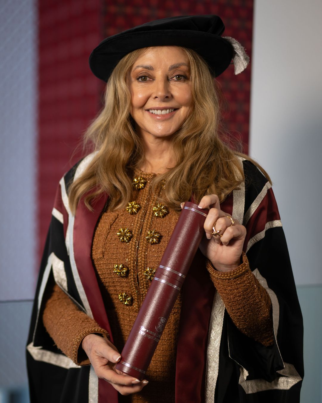 Lady in cap and gown holding a scroll smiling at the camera