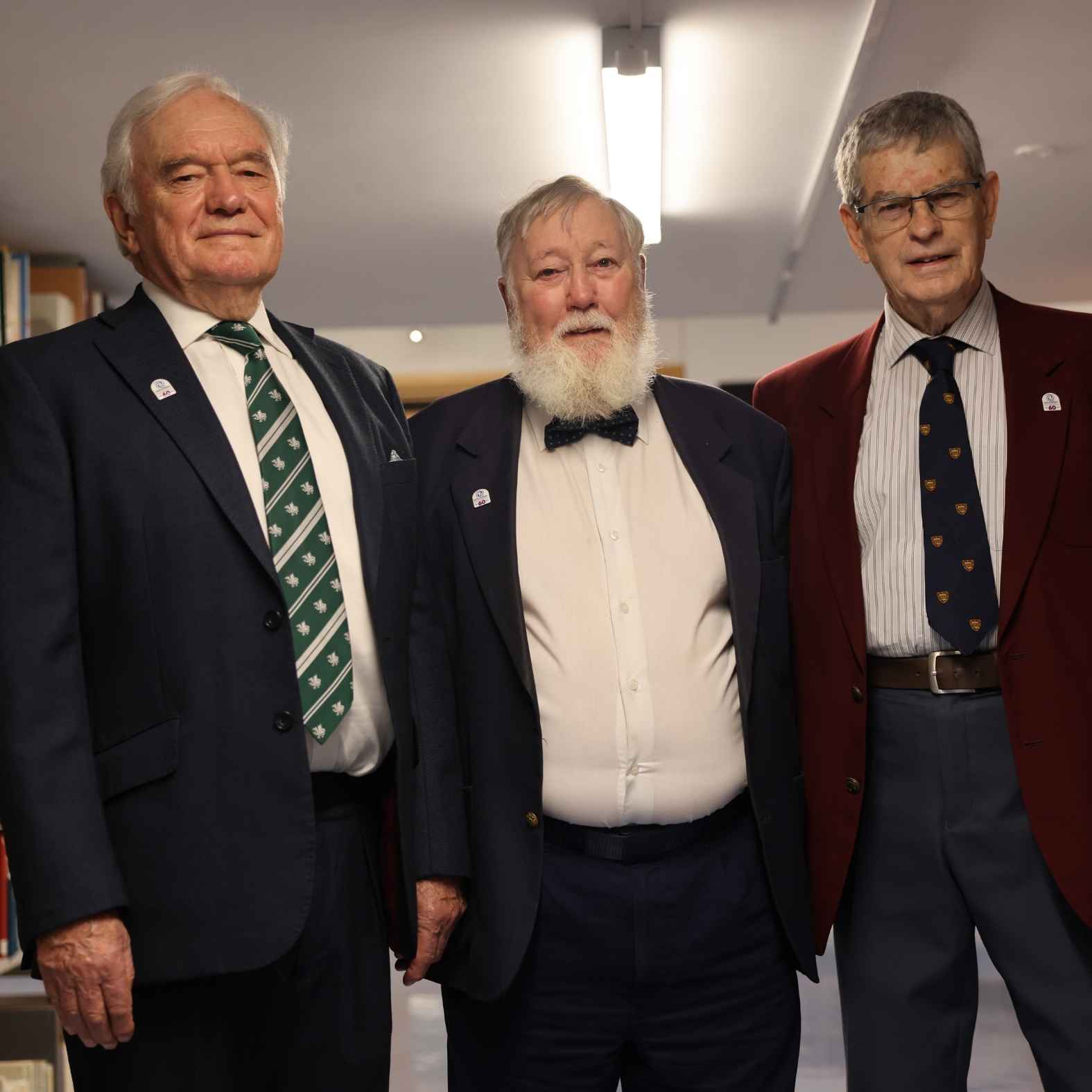 Three men wearing tuxedos standing in a row and smiling at the camera