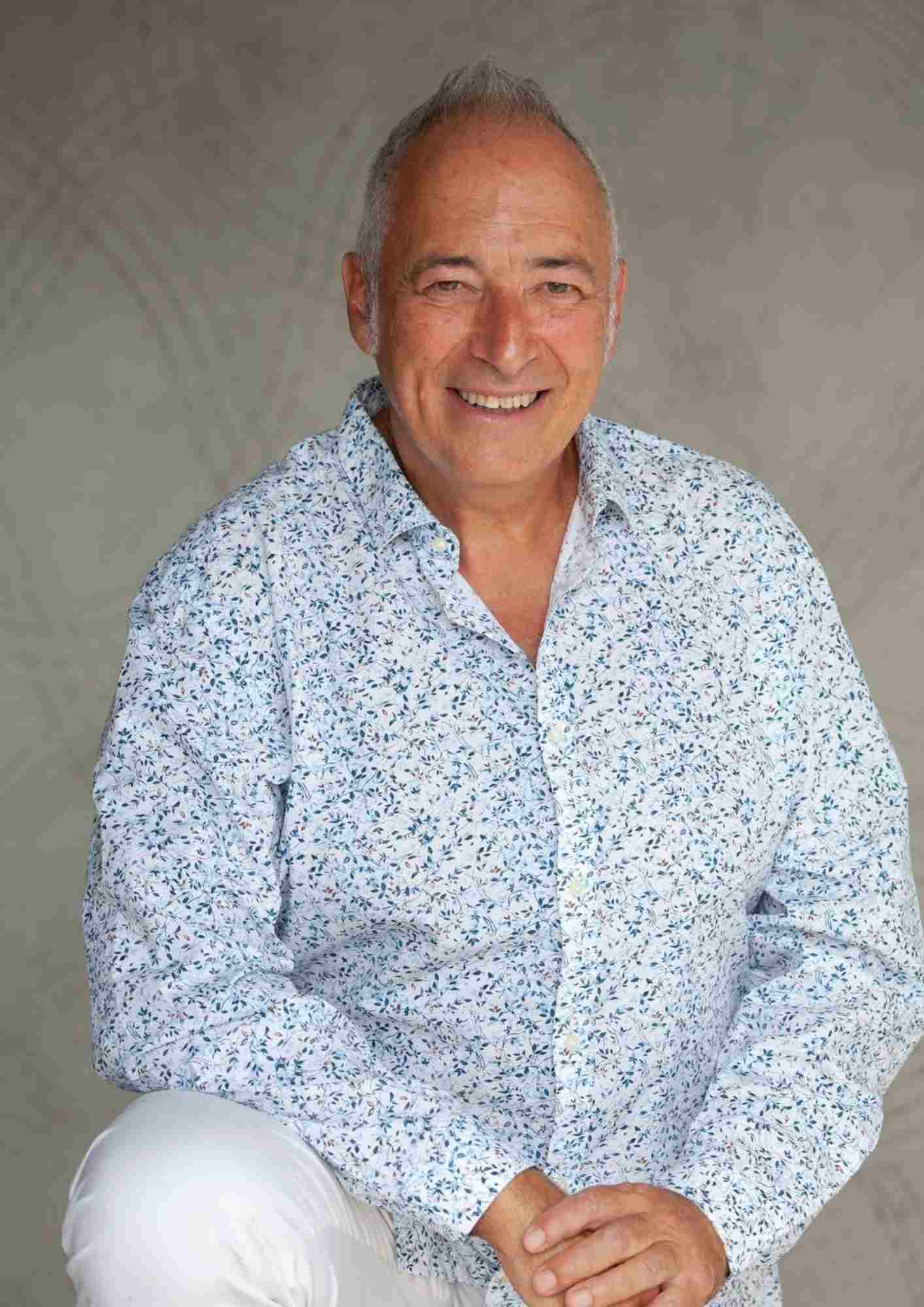 Gentleman wearing a blue and white shirt sitting down and smiling at the camera