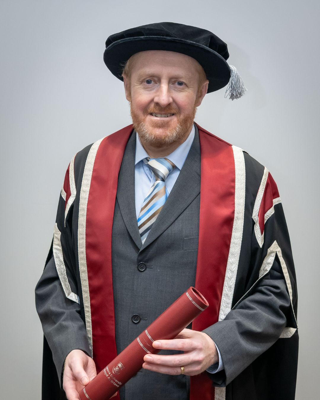 Man in cap and gown holding a scroll, smiling at the camera