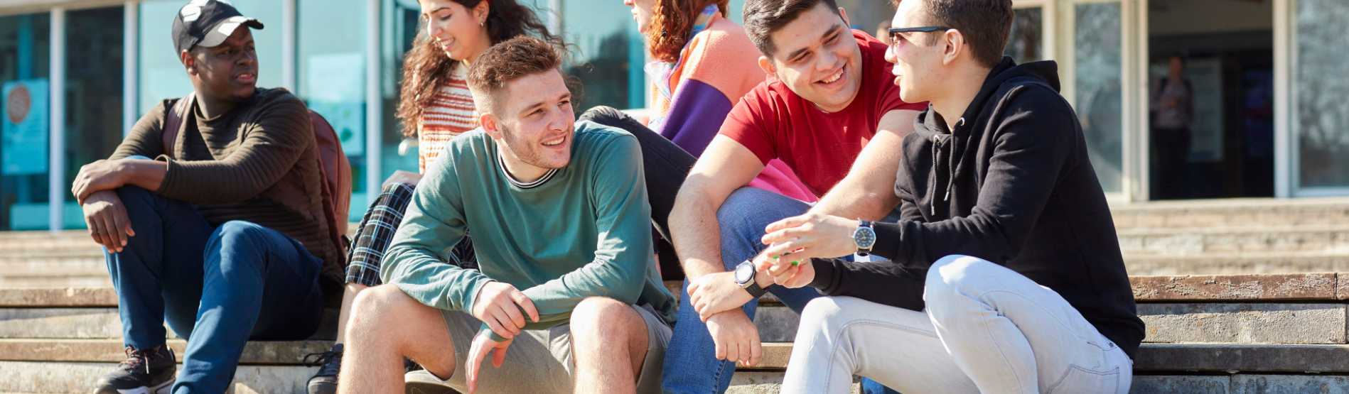 A group of students sitting on the steps of Fulton House smiling and chatting