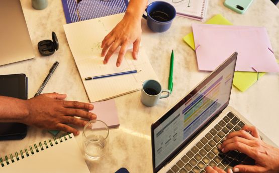 Laptops, paper & cups of coffee on a table with people working