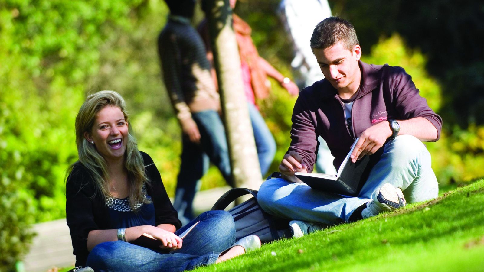 Students sitting on grass reading and smiling
