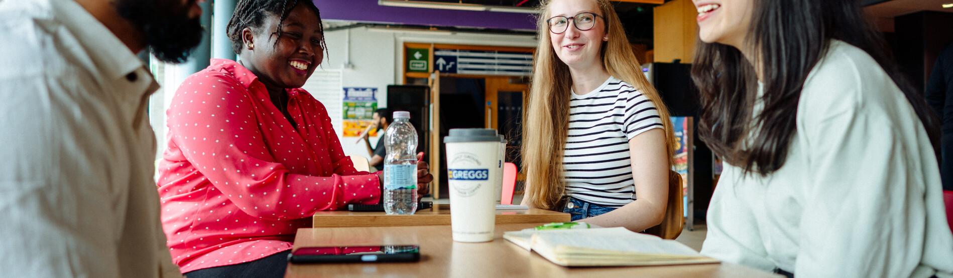 University students sat opposite each other on a table drinking coffee