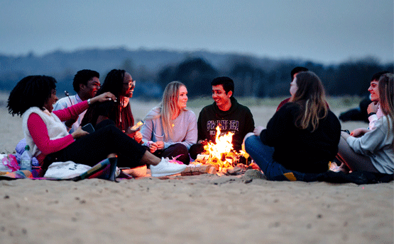 Group of students sat around a campfire on Swansea Bay in the evening
