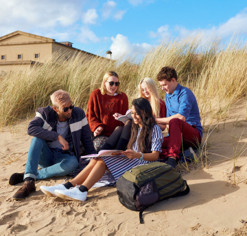An image of a group of students sitting on the beach next to the Bay Campus.