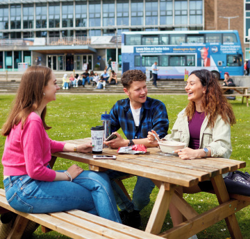 An image of a group of three students sitting at a table on the grass outside Fulton House on Singleton Campus.