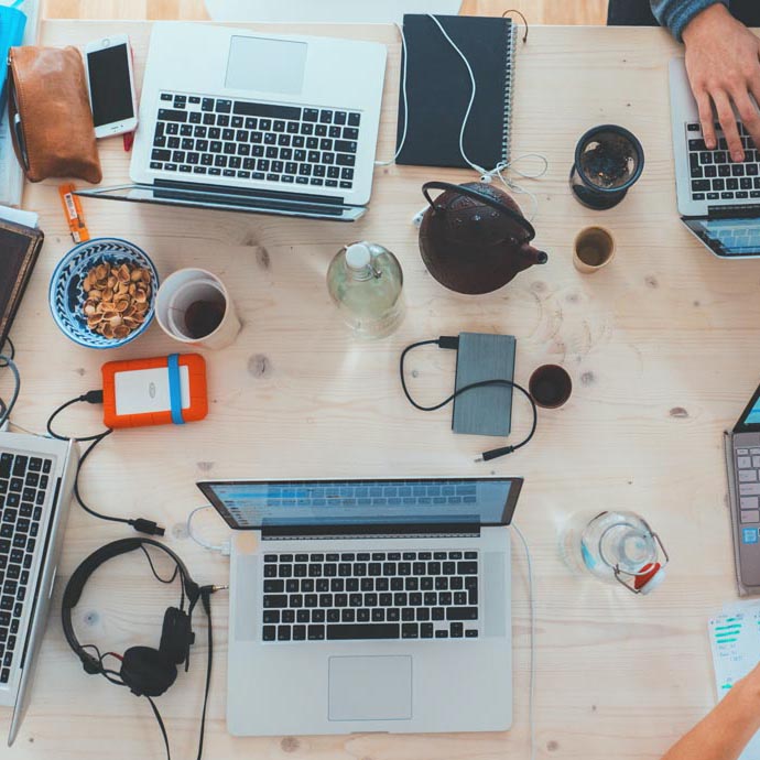 Image of a desk full of laptops, headphones and coffee mugs