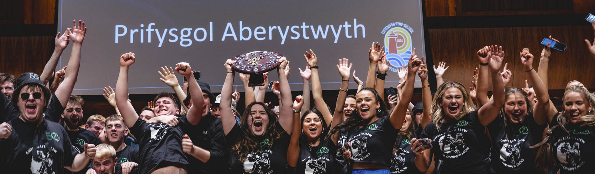 Myfyrwyr Prifysgol Aberystwyth yn codi'r tarian fuddugol