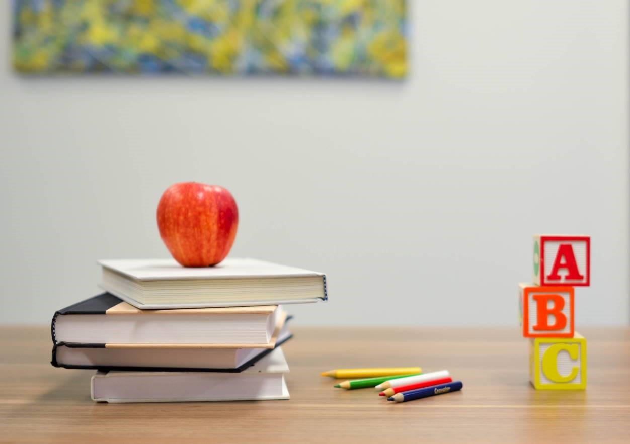 Shows a red apple sat on top of a pile of books. 