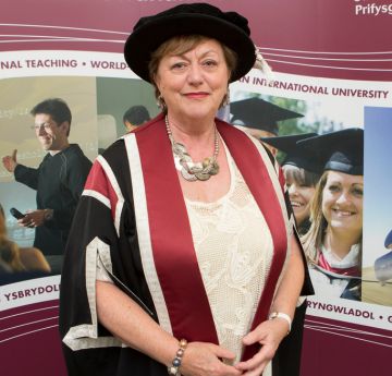 Lady wearing a cap and gown smiling at the camera