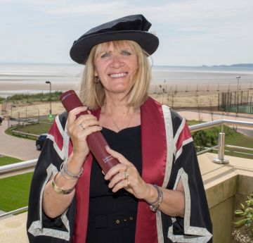 Menyw mewn gwisg graddio yn gwenu i'r camera