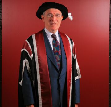 Dyn y gwisgo gwisg graddio yn gwenu wrth y camera