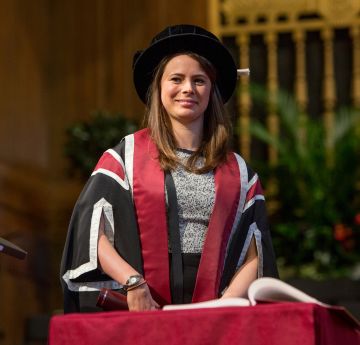 Menyw yn gwisgo gwisg graddio yn arwyddo llyfr