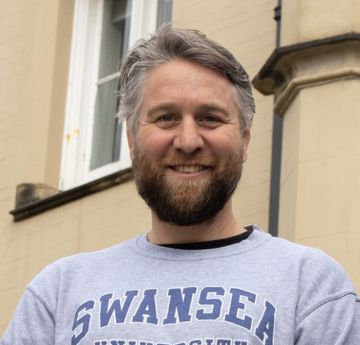 Man wearing a Swansea University jumper smiling at the camera