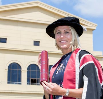 Menyw mewn gwisg graddio yn gwenu i'r camera
