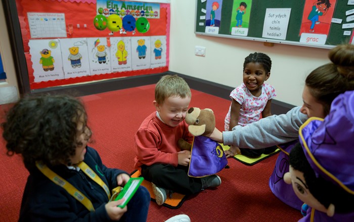 Plant yn chwerthin wrth chwarae gyda’r teganau anwes Doti a Dewin mewn un o gylchoedd chwarae Mudiad Meithrin.