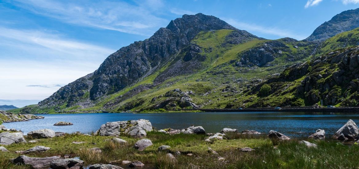 Ardal o ddŵr mewndirol gyda chreigiau a mynydd yn y cefndir yn erbyn awyr las