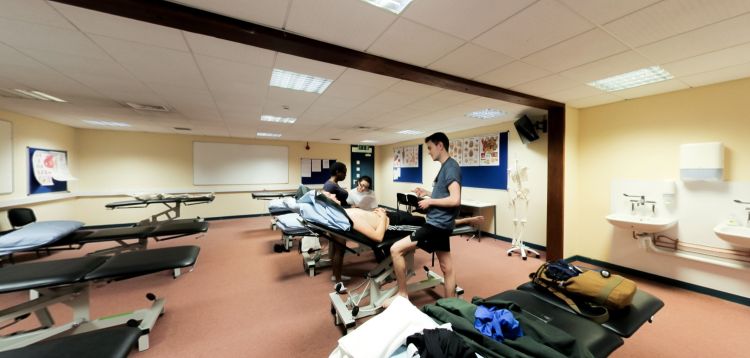 Ystafell ymarfer osteopathig gyda byrddau triniaeth a sesiwn hyfforddiant clinigol