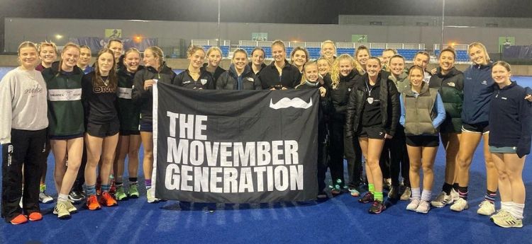 Hockey players holding a Movember flag on the hockey field after their triple header movember hockey fixture.
