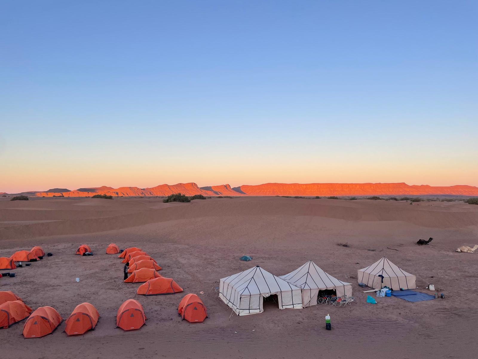 Tents in desert with mountains and sunset in distance