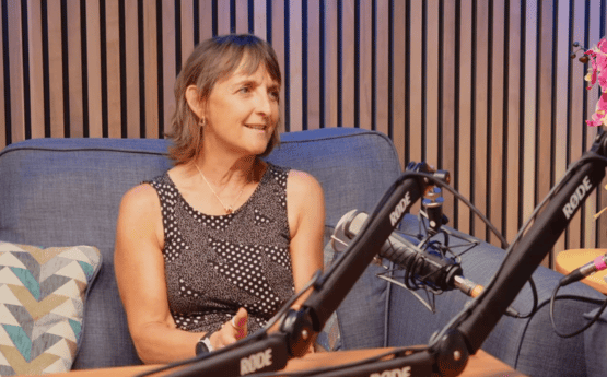 A woman sitting on a grey sofa speaking into a microphone for a podcast.