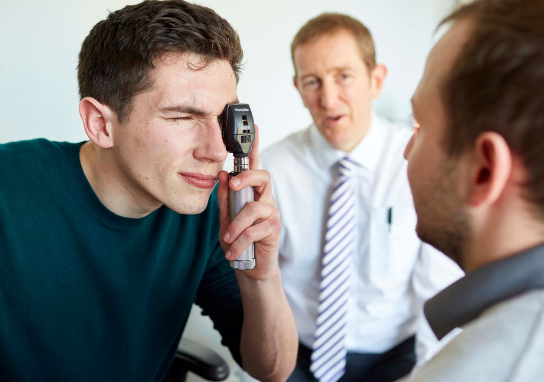 Student examining a patient's eye under the watch of a medical supervisor