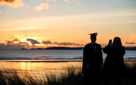 sunset over Swansea bay with graduate in front.