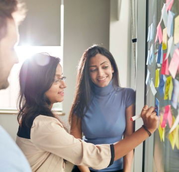 Three members of staff arranging sticky notes on a glass wall