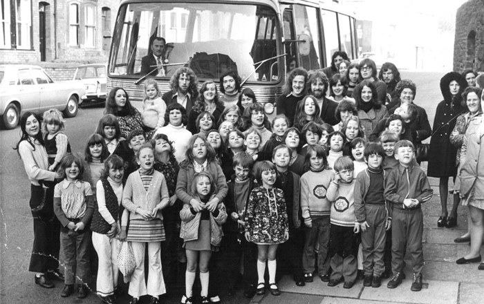 A large group of student volunteers standing in front o a large bus in the 60s