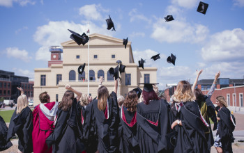 Students celebrate their graduation by throwing mortarboards in the air.