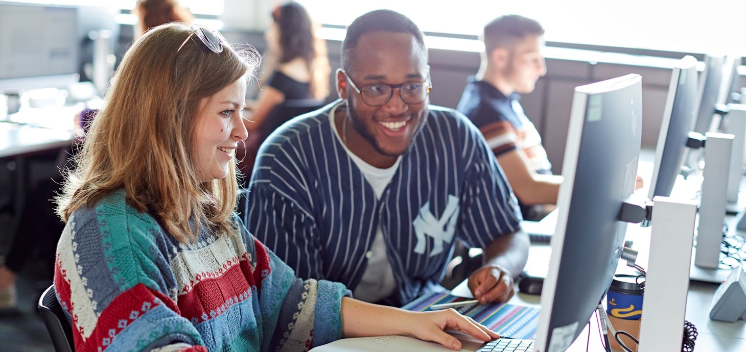 Two students sitting working in a computer lab.