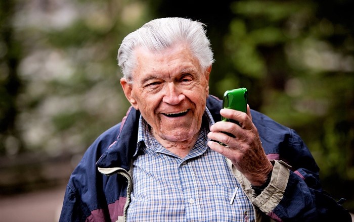 An older man holding a mobile phone and smiling