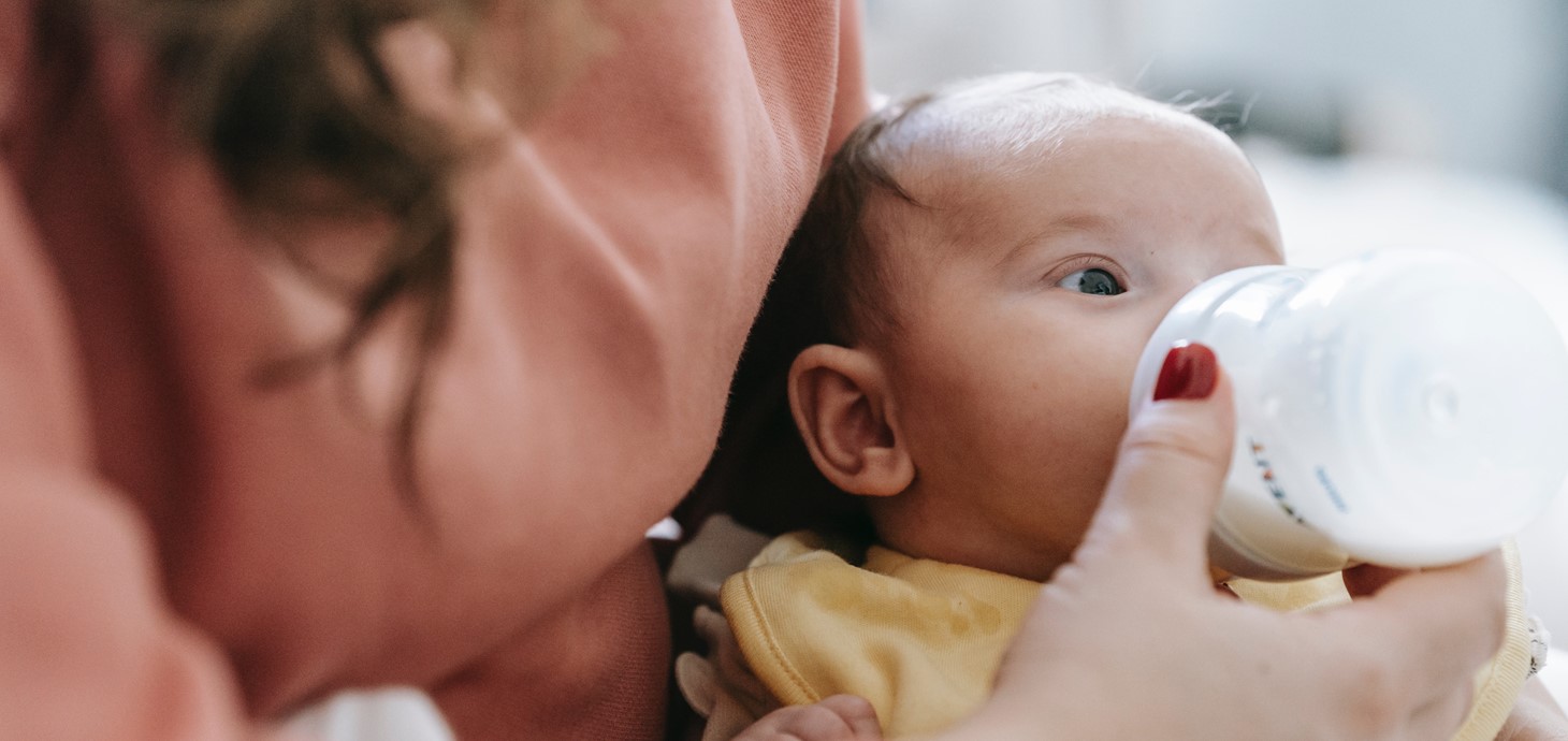 Mother feeding infant with milk from a bottle.