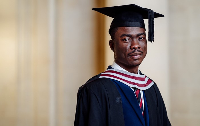 A photo of Martin Tarkpor on his graduation day. Martin is wearing a blue suit and his graduation cap and gown.