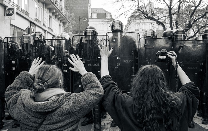 Two protestors - one with a camera - in front of a police line at a Paris demonstration against a new security law, December 2020. Credit: Koshu Kunii on Unsplash