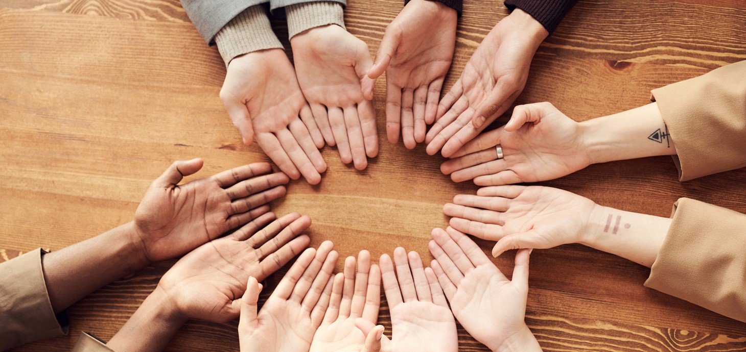 Picture of six pairs of hands held out palms upwards in a circle on table