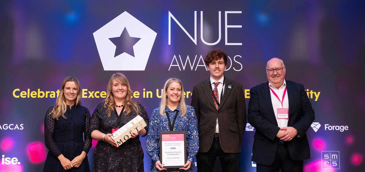 Three women and two men standing in a row at an awards ceremony.