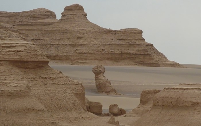 View across Gobi Desert with sand in foreground and mountains in the distance.