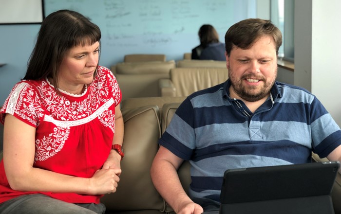 Man and woman sitting on a sofa looking at a laptop being held by the man.