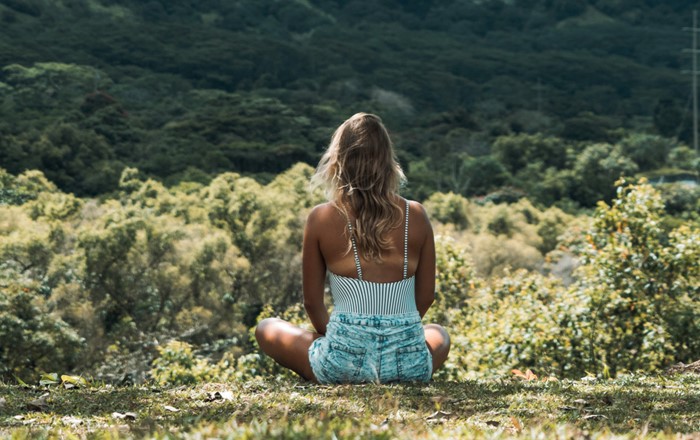 Woman sitting outside in the countryside with her back to the camera