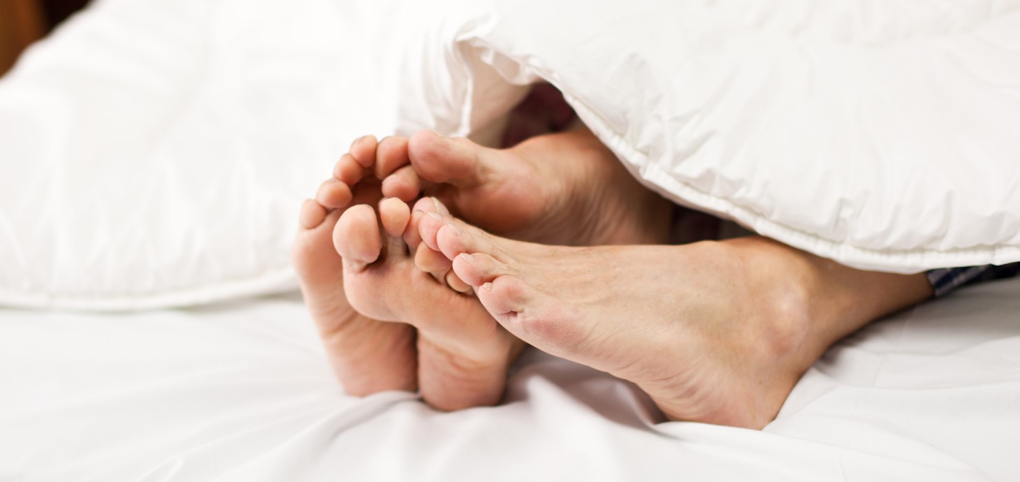 A pair of men's and women's feet sticking out at the end of a white duvet