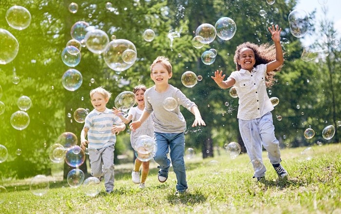 Smiling children running across grass chasing bubbles