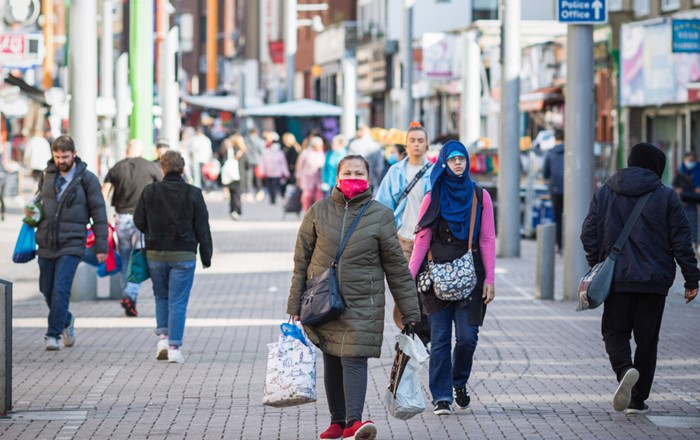 Woman wearing a facemask front and centre walking along a pedestrianised shopping street with other people in background 